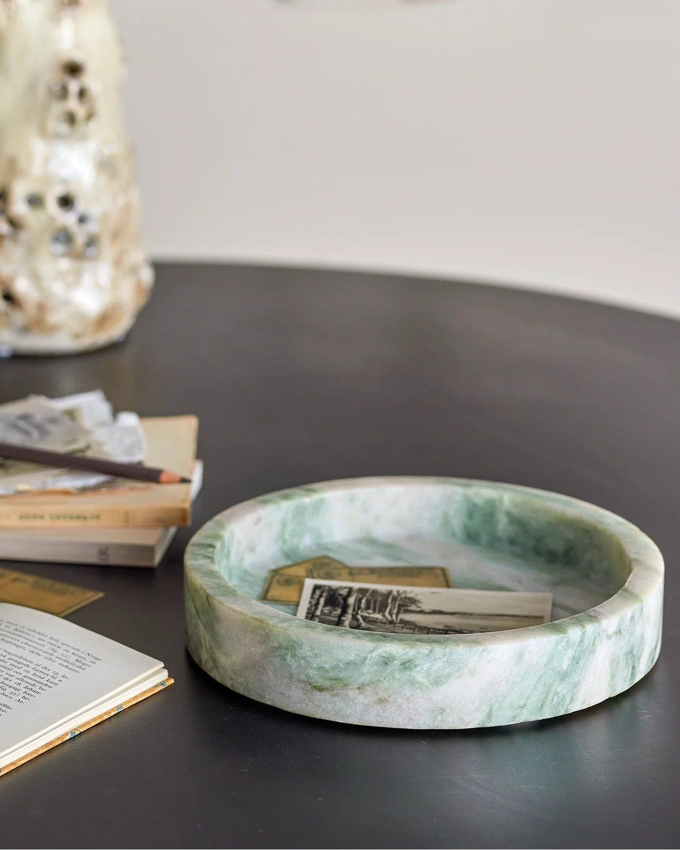 Green marble dish on a dark surface with books and a vase in the background