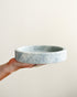 Hand holding a marble-patterned ceramic bowl against a plain background
