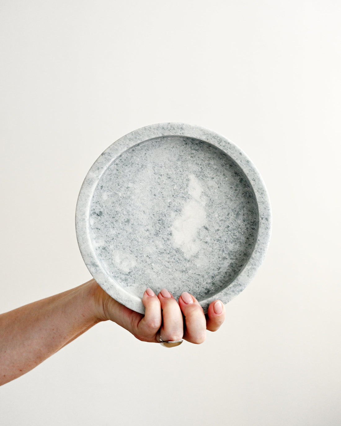 Hand holding a gray speckled ceramic plate against a plain background