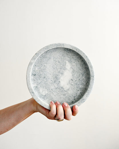 Hand holding a gray speckled ceramic plate against a plain background