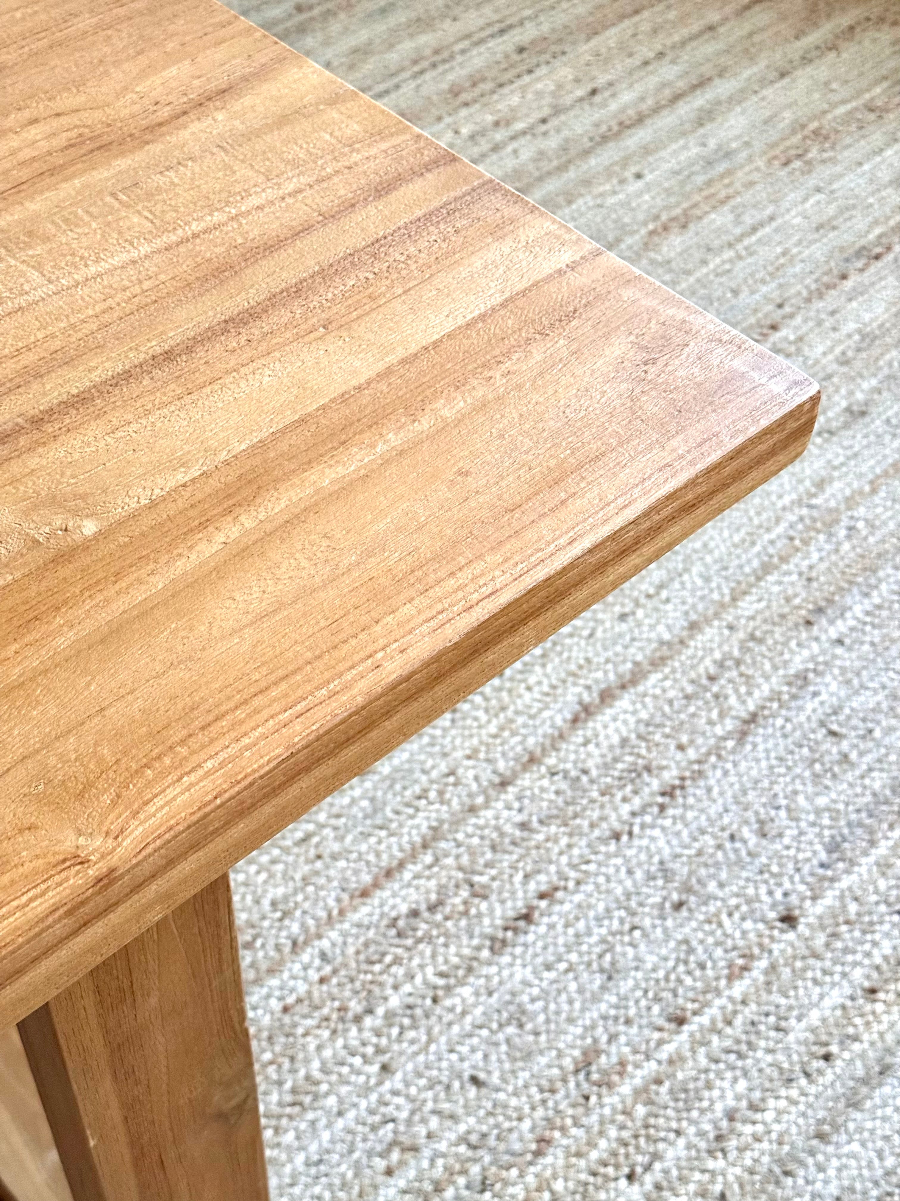 Close-up of a light natural wood tabletop corner with a matching wooden leg, placed on a woven beige rug.