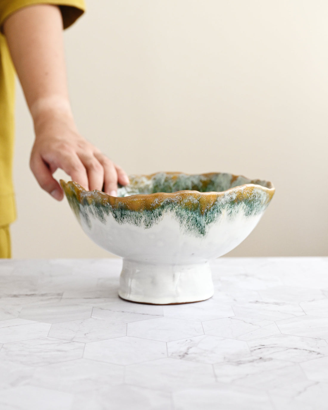Ceramic bowl with a textured edge on a marble surface, held by a person wearing a yellow shirt.