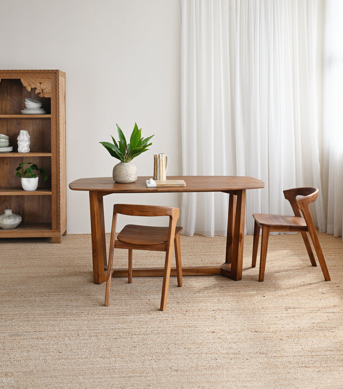 Dining area with wooden table and chairs in a room with white walls and curtains.