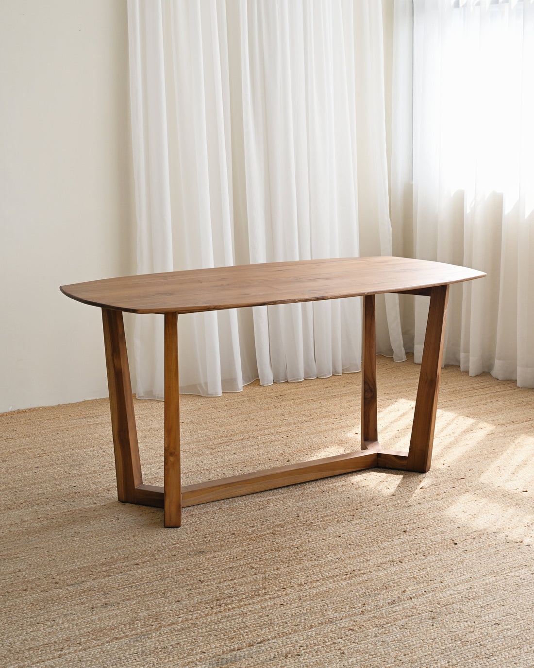 Wooden table in a room with light-colored curtains and wooden floor.