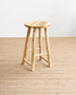 Wooden stool on a textured beige floor with a light gray wall background