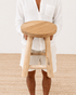 Person holding a wooden stool on a neutral background