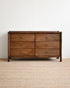 Wooden dresser with four drawers on a beige carpet and white wall background