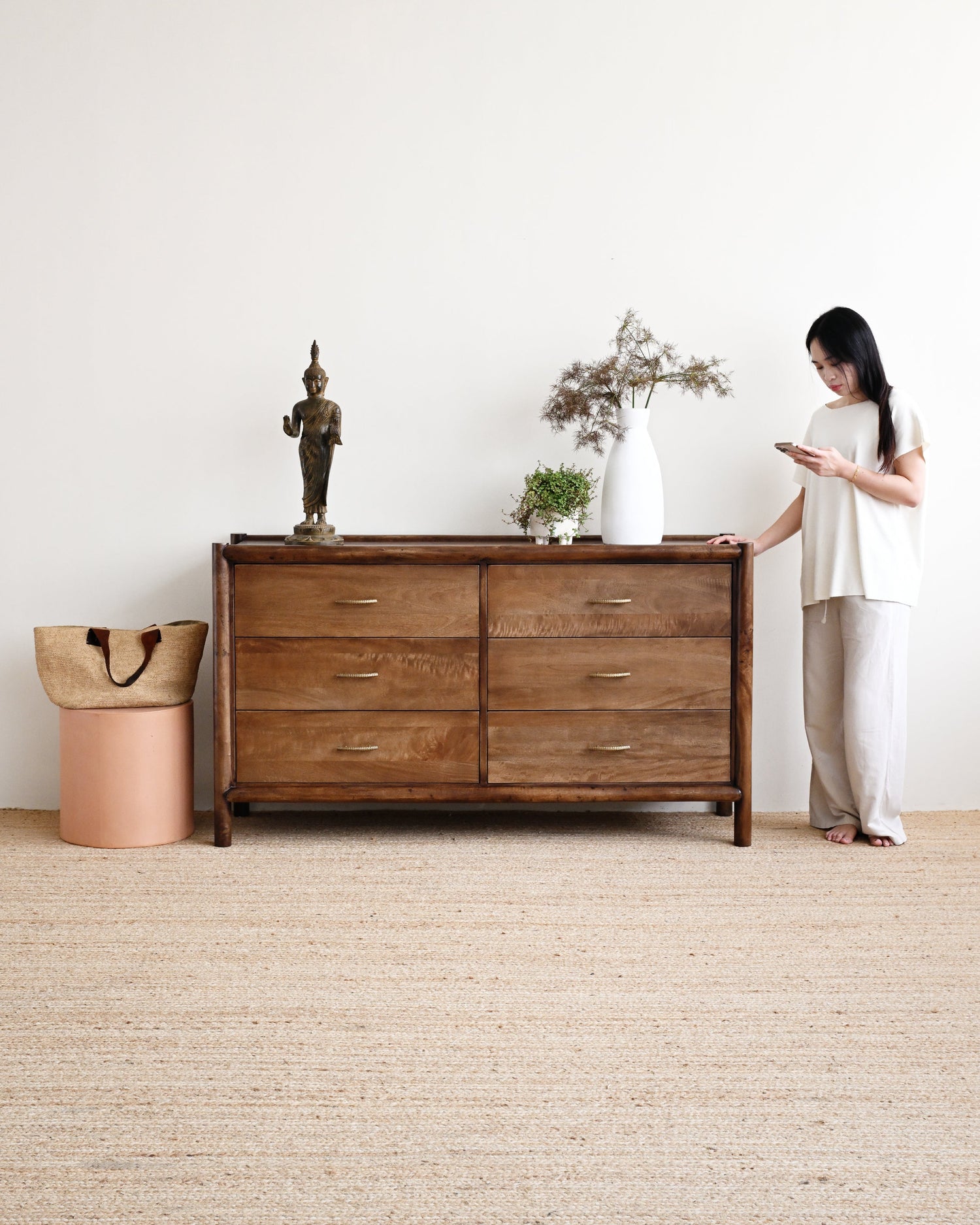 Woman standing next to a wooden dresser in a minimalistic room.