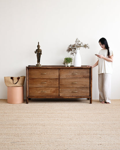 Woman standing next to a wooden dresser in a minimalistic room.
