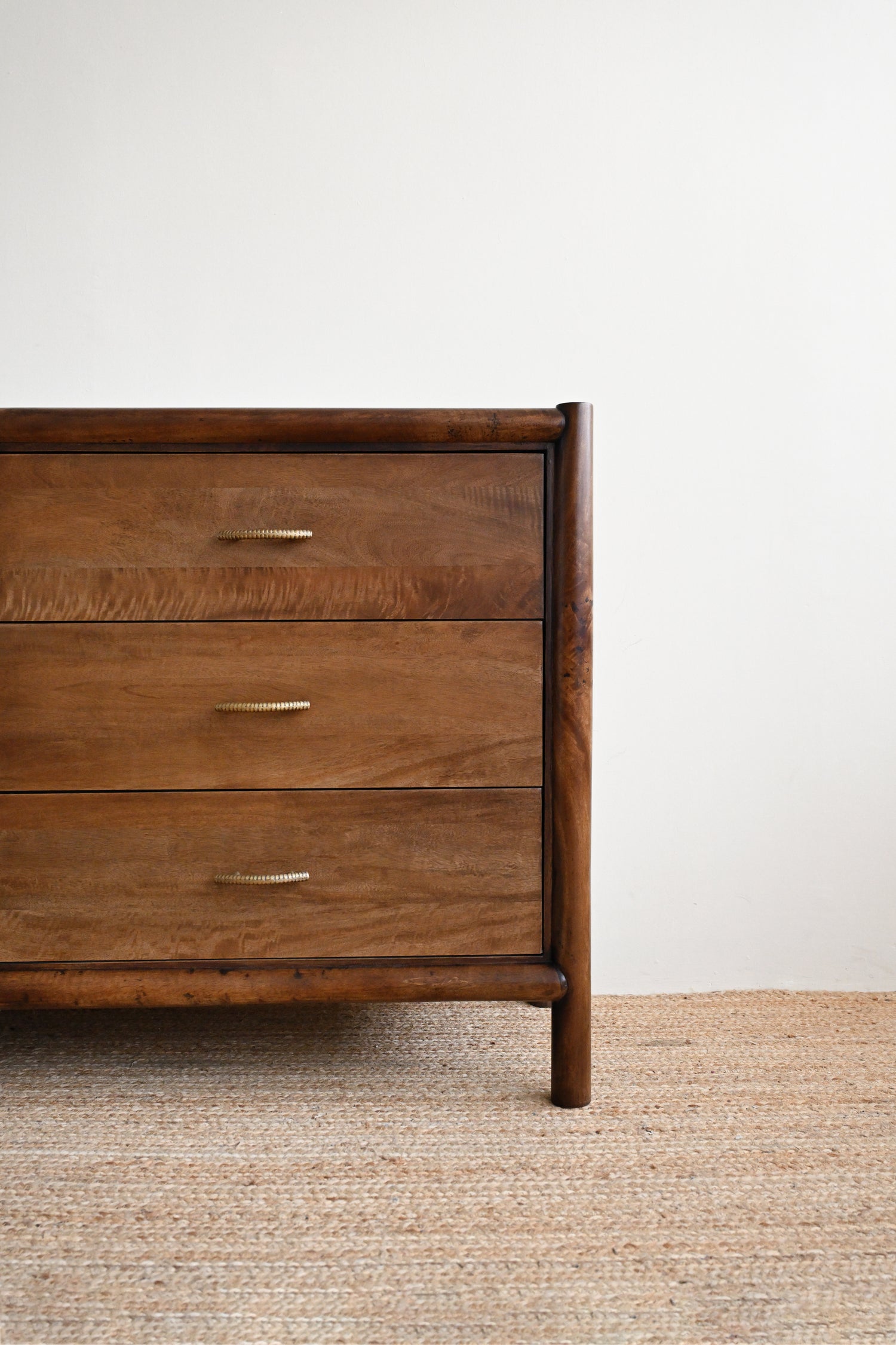 Wooden dresser with three drawers on a textured floor against a white wall