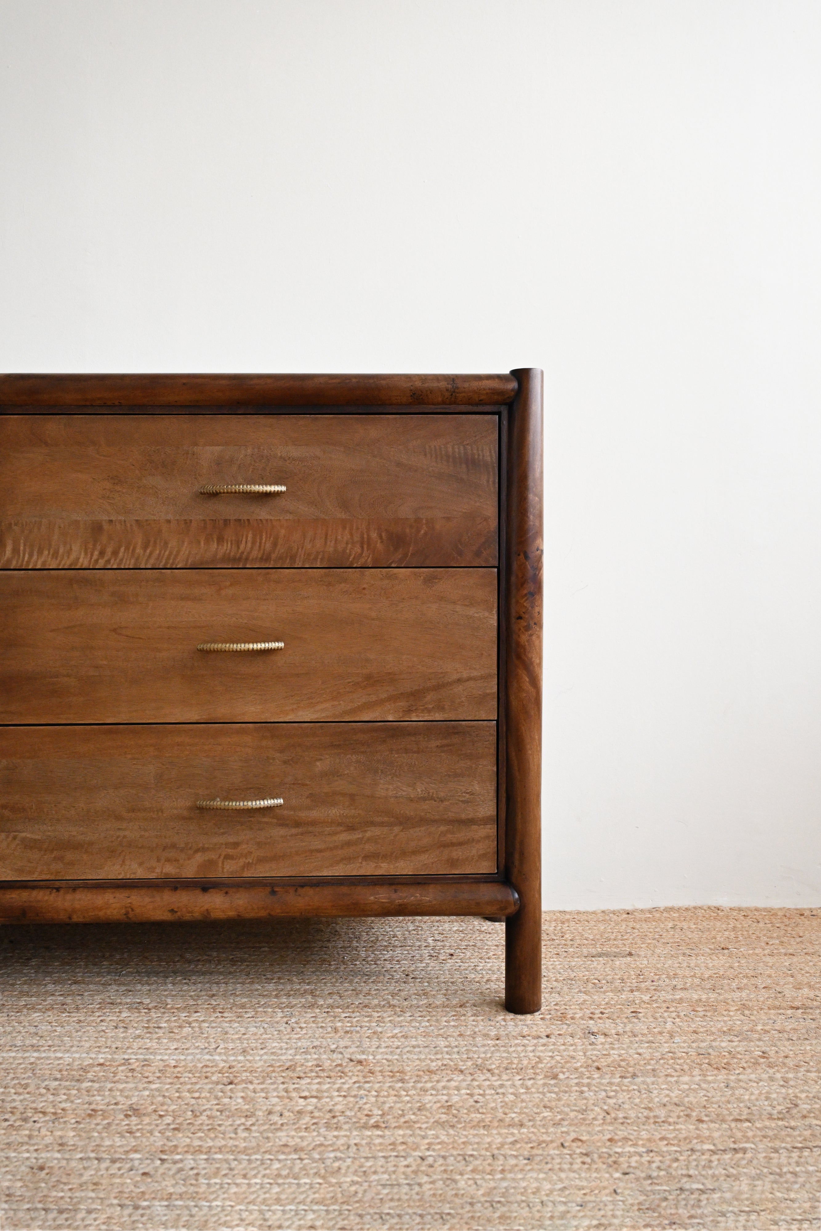 Wooden dresser with three drawers on a textured floor against a white wall
