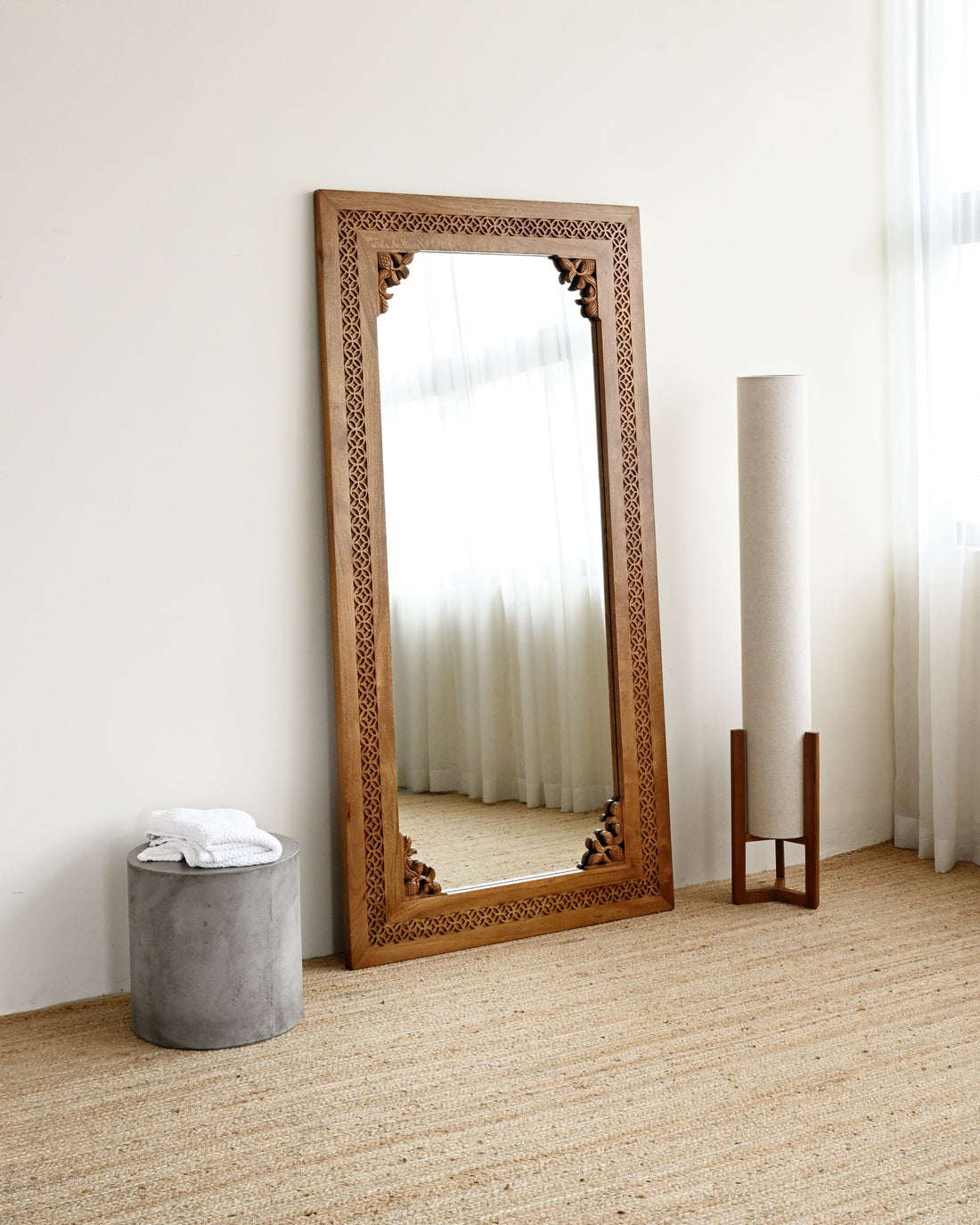 Wooden floor mirror with decorative frame leaning against a white wall.