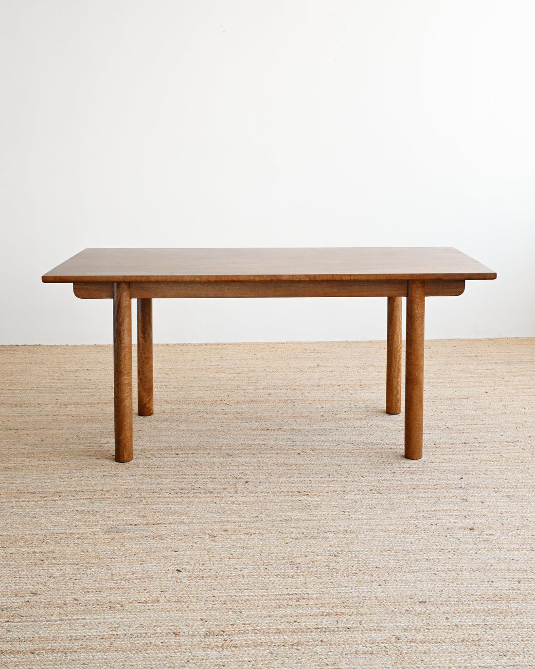 A mid-century modern wooden coffee table with a rectangular top and four tapered legs, shown on a textured beige woven rug against a plain white wall.