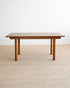 A mid-century modern wooden coffee table with a rectangular top and four tapered legs, shown on a textured beige woven rug against a plain white wall.