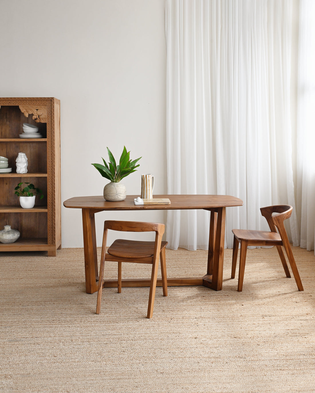 Dining area with wooden table and chairs in a room with white walls and curtains.