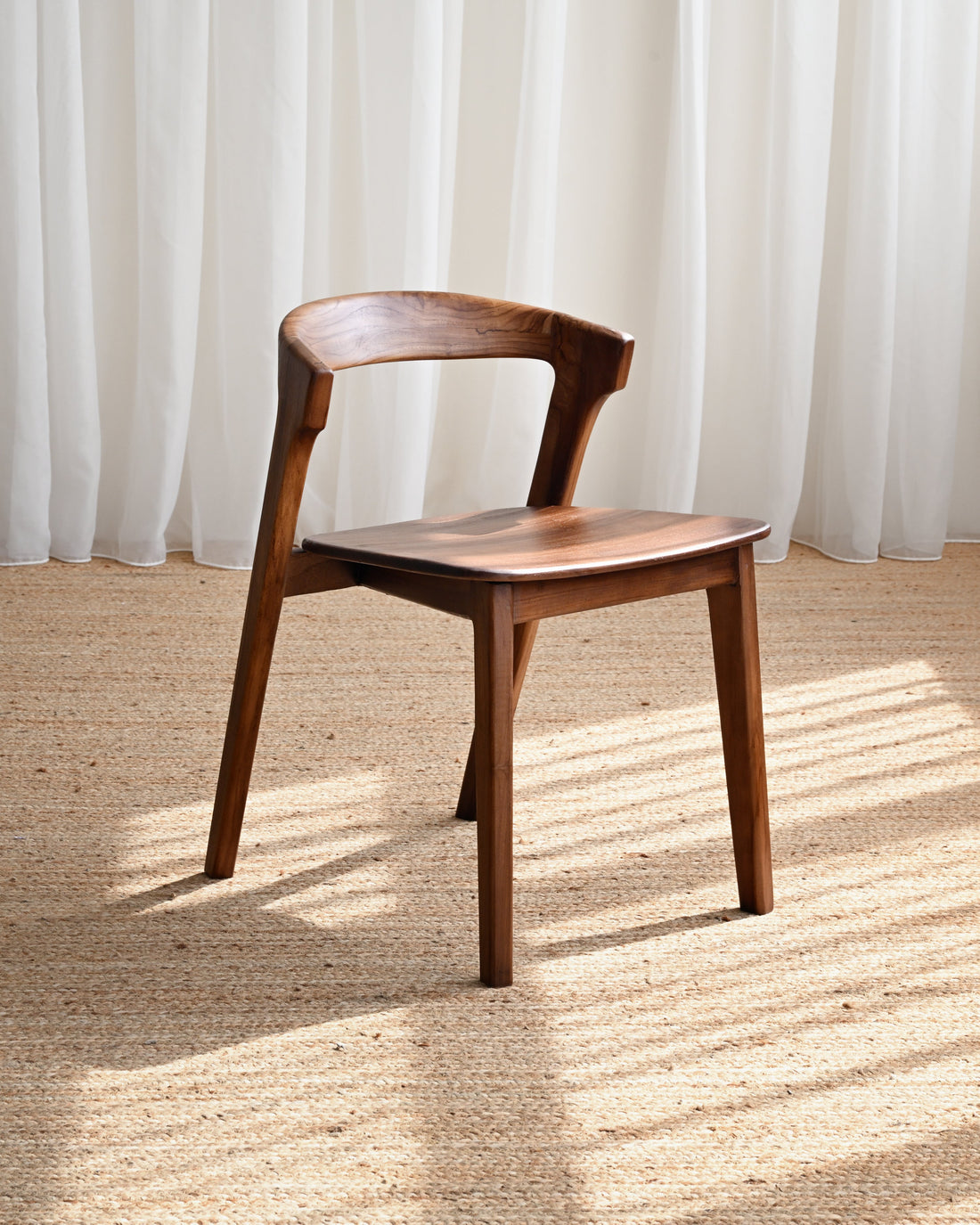 Wooden chair on a textured floor with white curtains in the background