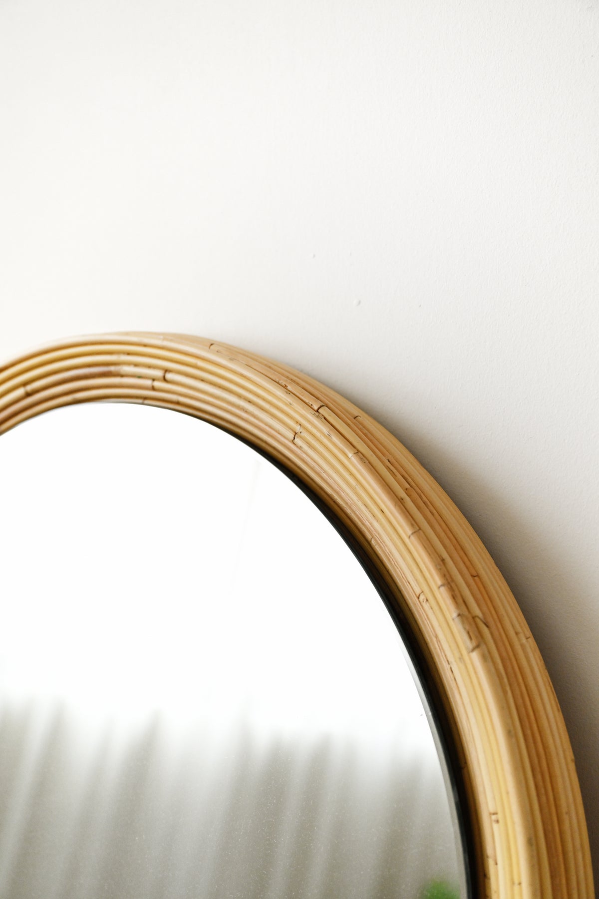 A close-up of a round mirror with a natural light wood or rattan frame against a plain white wall.
