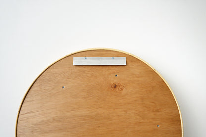 Close-up of the back of a round wooden wall art piece, showing a natural wood grain surface, a metal mounting plate with screws, and a thin wooden edge against a plain white background.