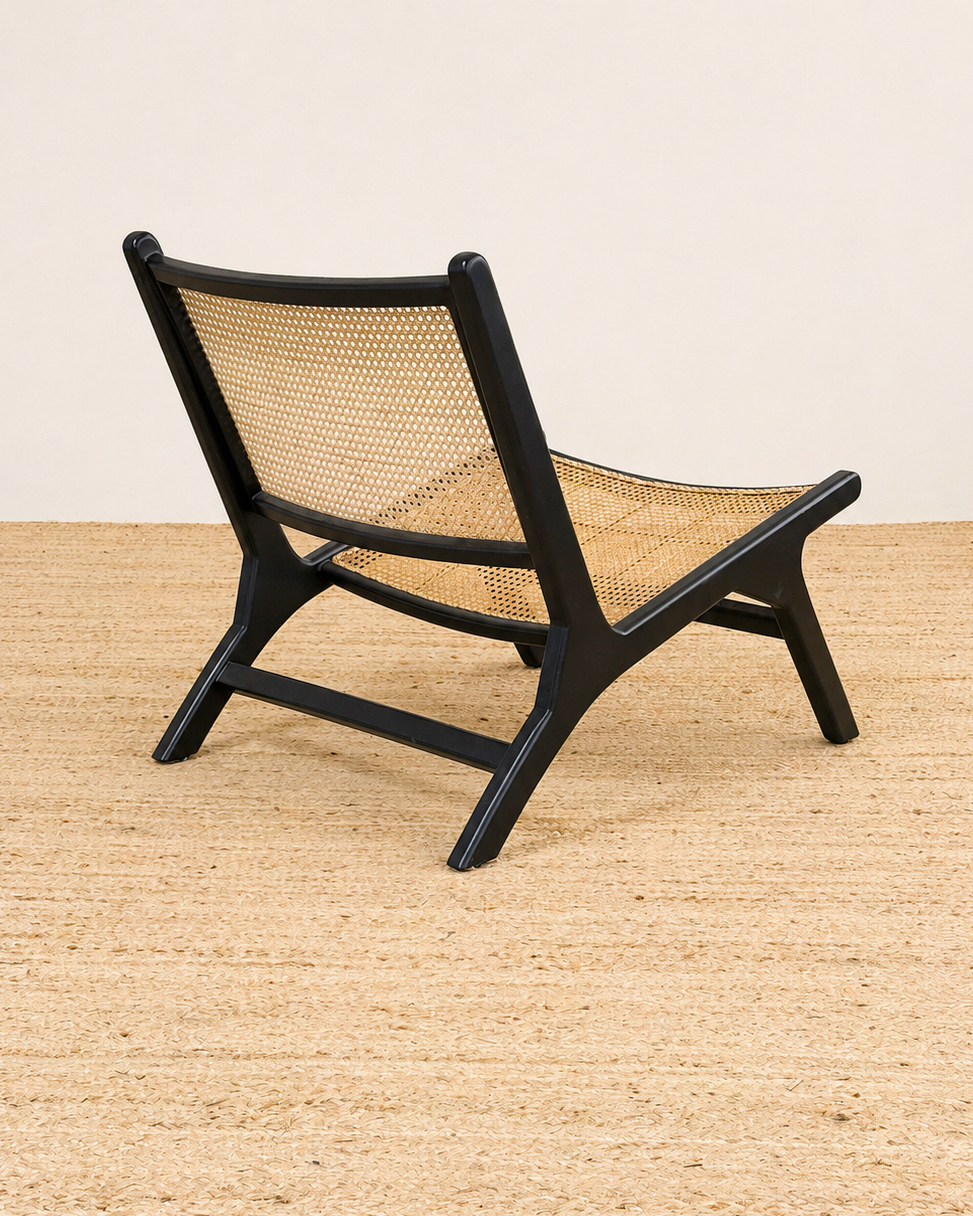 Modern lounge chair with black frame and woven backrest on a beige floor.
