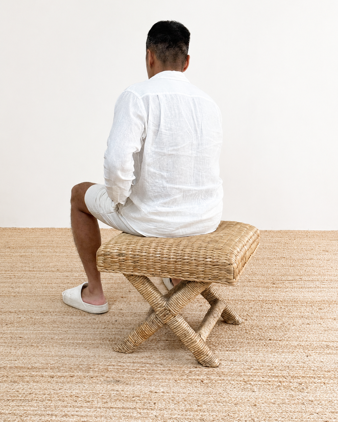 Person sitting on a woven stool in a minimalistic setting