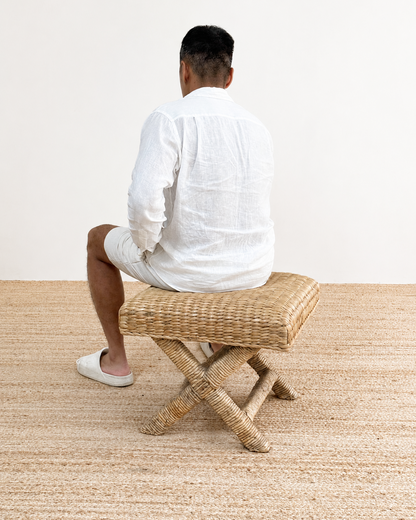 Person sitting on a woven stool in a minimalistic setting