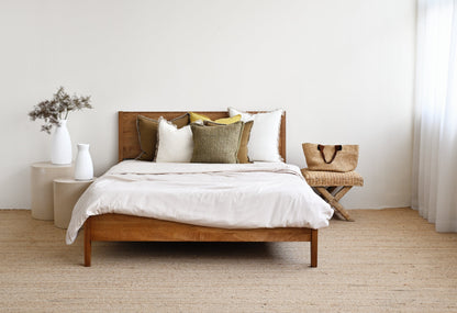 Wooden bed with white bedding and pillows in a minimalistic bedroom.
