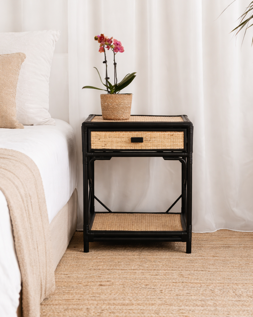 Bedroom with a nightstand featuring a plant and a basket, against a white curtain backdrop.
