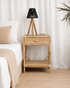 rattan nightstand with black lamp next to a bed in a bedroom setting
