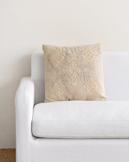 Beige pillow with lace detailing on a white sofa against a beige wall