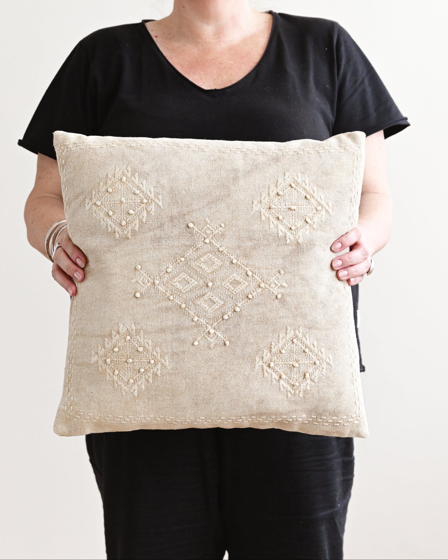 Person holding a decorative pillow with intricate patterns against a plain background