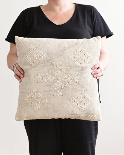 Person holding a decorative pillow with intricate patterns against a plain background
