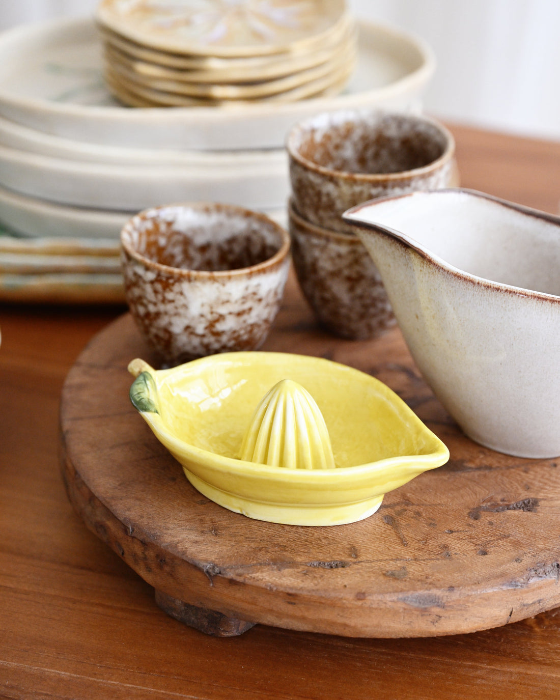 Yellow lemon squeezer on a wooden surface with ceramic bowls and plates in the background.
