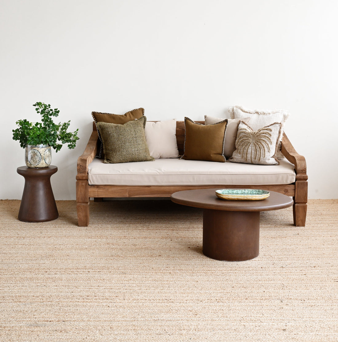 Modern living room with a wooden sofa, round coffee table, and decorative pillows on a light-colored carpet.