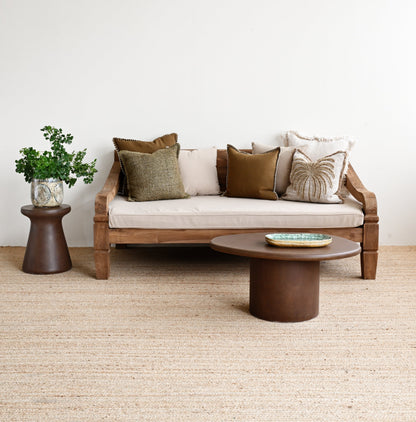 Modern living room with a wooden sofa, round coffee table, and decorative pillows on a light-colored carpet.