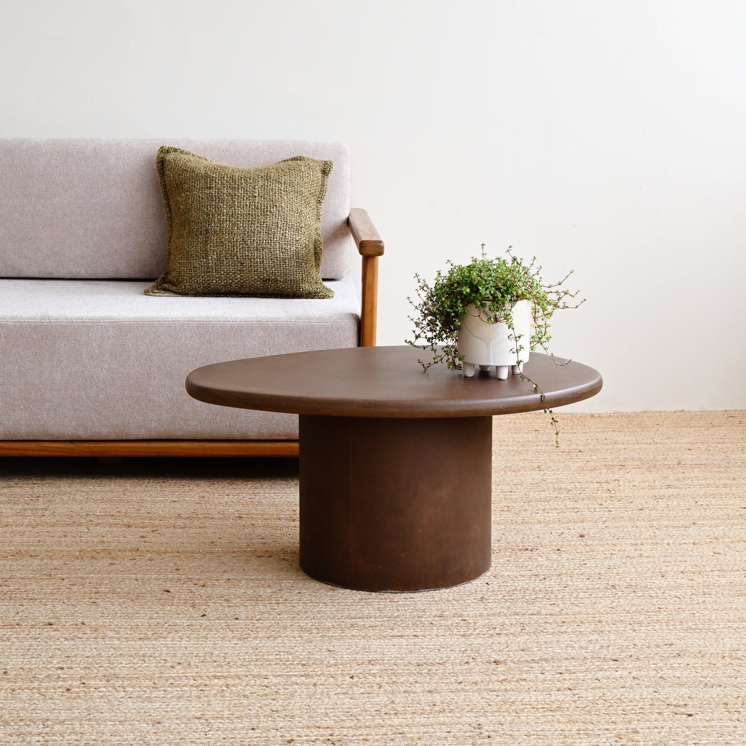 Sofa with a pillow and a round wooden table in a room with a white wall and beige carpet.