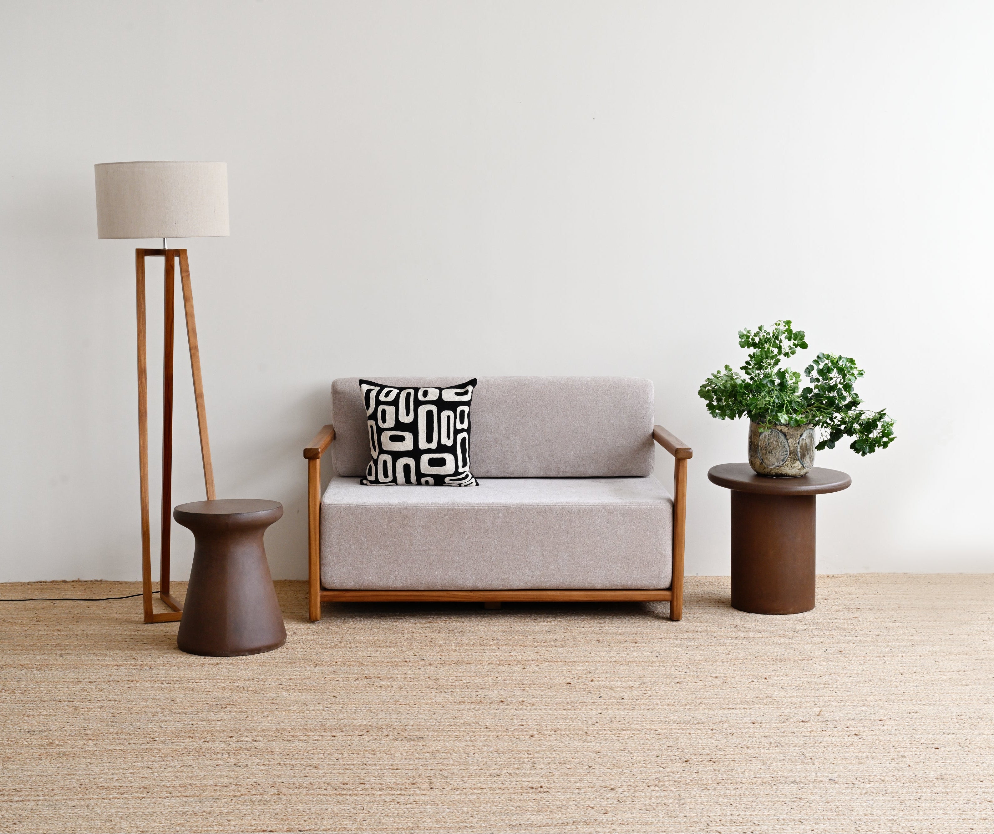 Gray sofa with a patterned pillow, standing lamp, and small table with a plant in a minimalistic room.