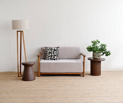 Gray sofa with a patterned pillow, standing lamp, and small table with a plant in a minimalistic room.