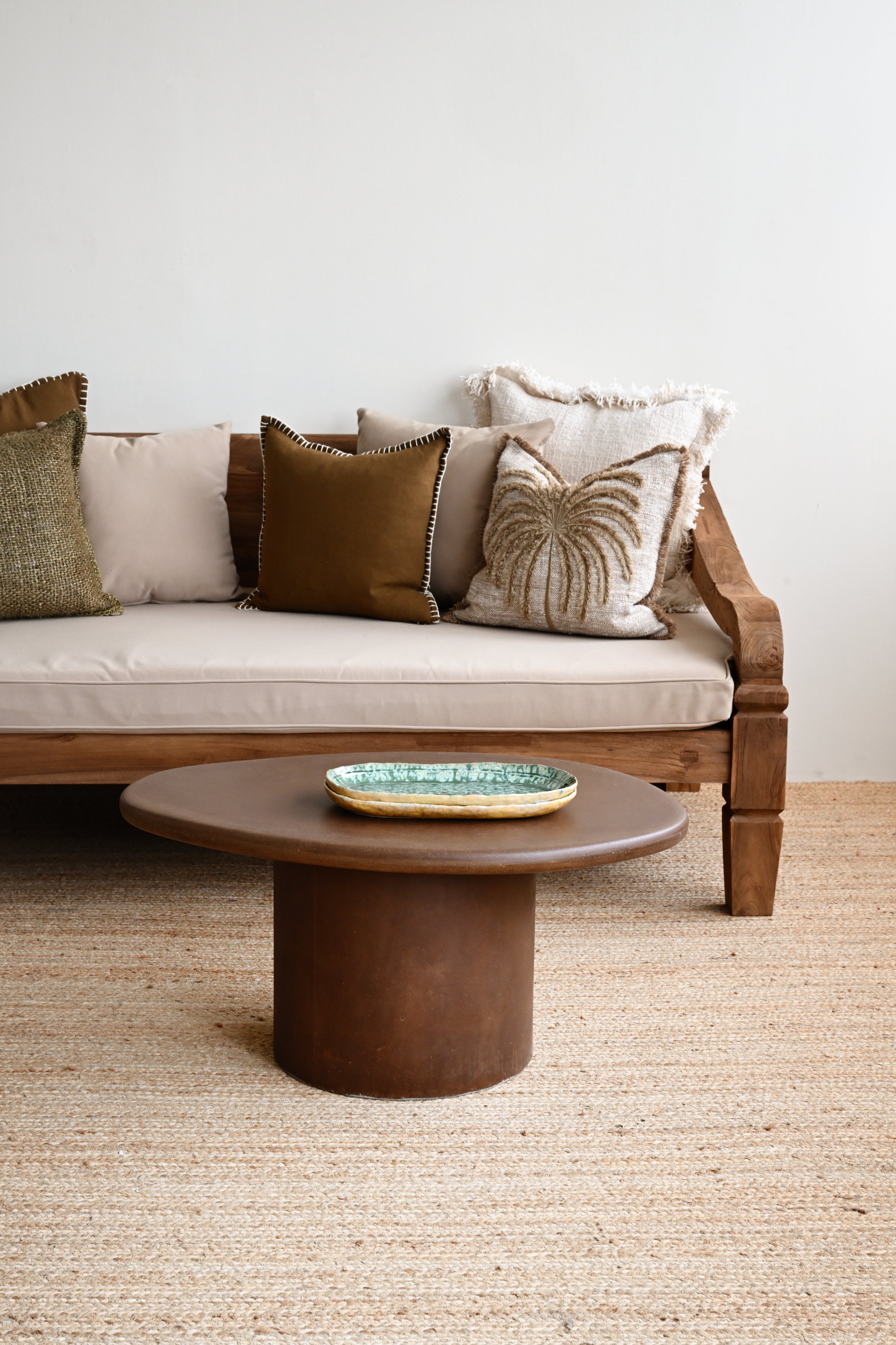Wooden sofa with decorative pillows and a round wooden table in a living room setting.