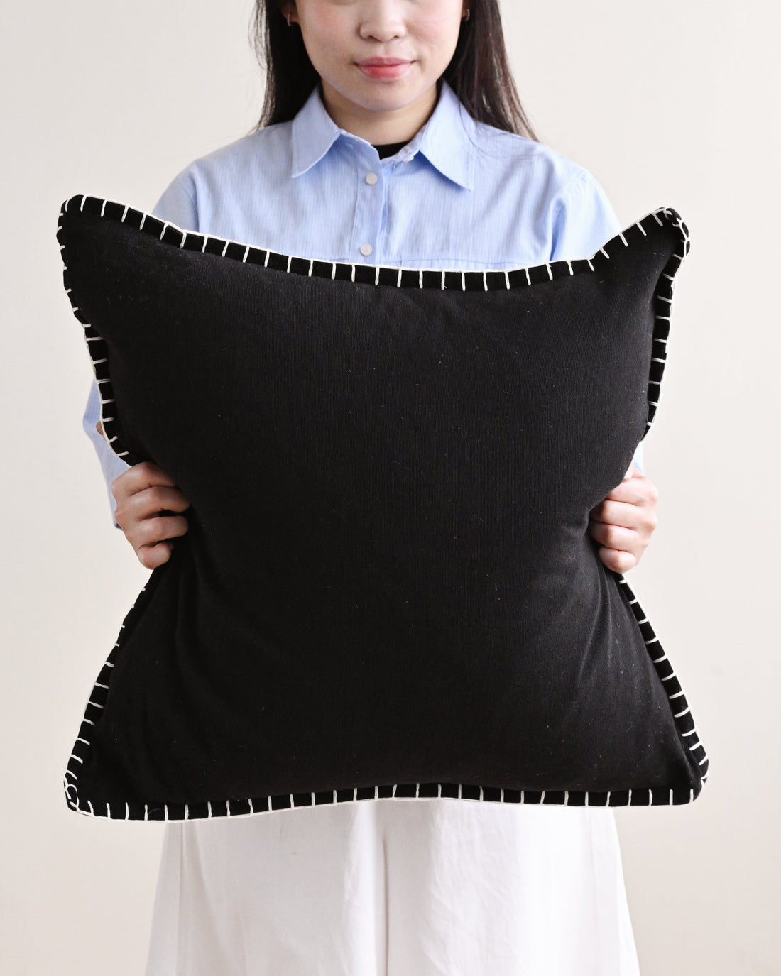 Person holding a large black pillow with white trim against a plain background