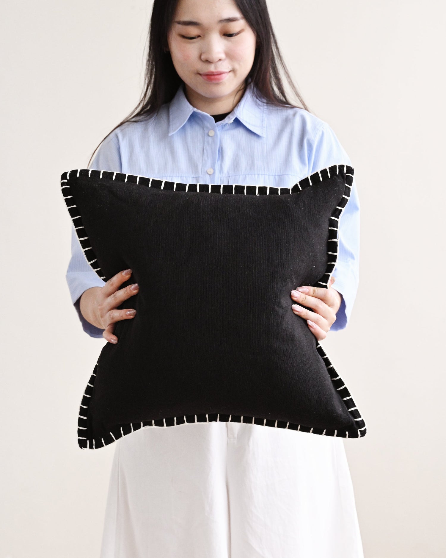 Person holding a black pillow with white trim against a plain background