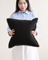 Person holding a black pillow with white trim against a plain background