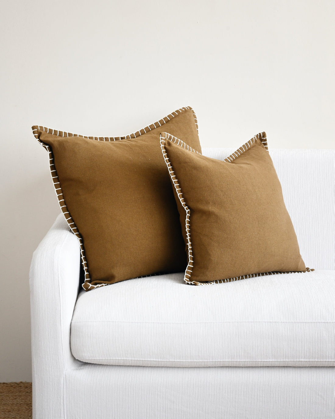 Two brown pillows on a white couch against a light gray wall