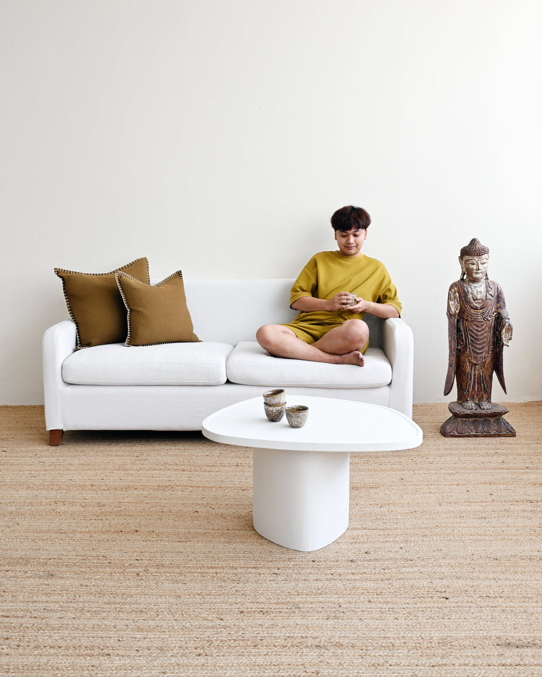 Person sitting on a white sofa with gold cushions in a minimalistic room.