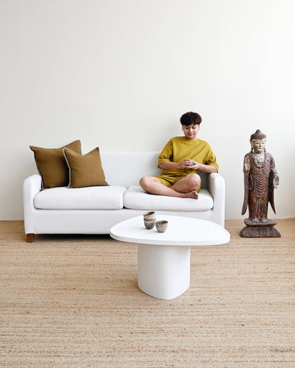 Person sitting on a white sofa with gold cushions in a minimalistic room.