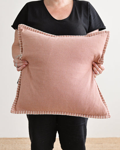 Person holding a large pink pillow against a plain background