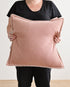 Person holding a large pink pillow against a plain background