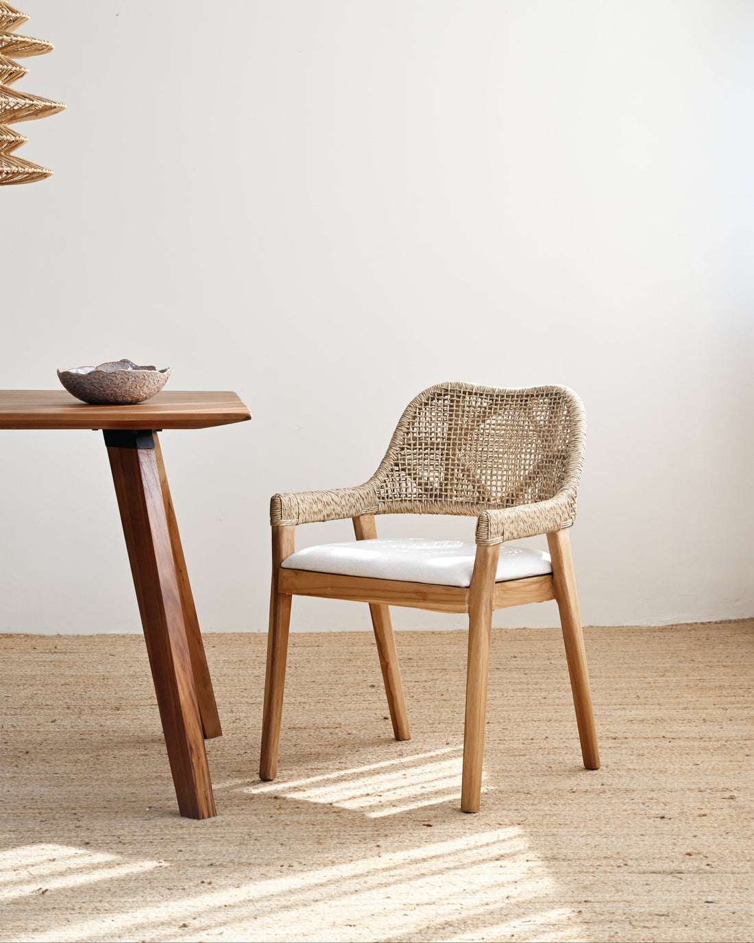 Woven chair and wooden table against a white wall