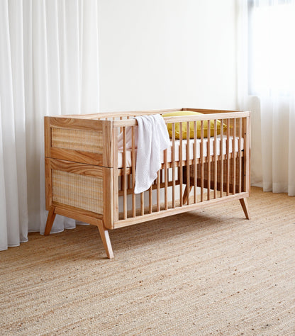 Wooden crib with a white blanket in a room with light-colored carpet and curtains.