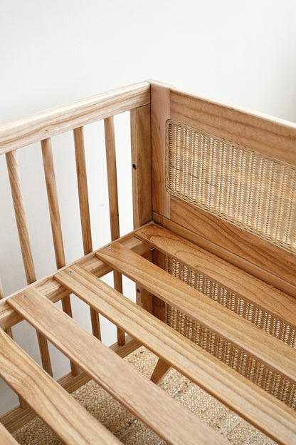 Wooden crib with wicker backrest against a white wall