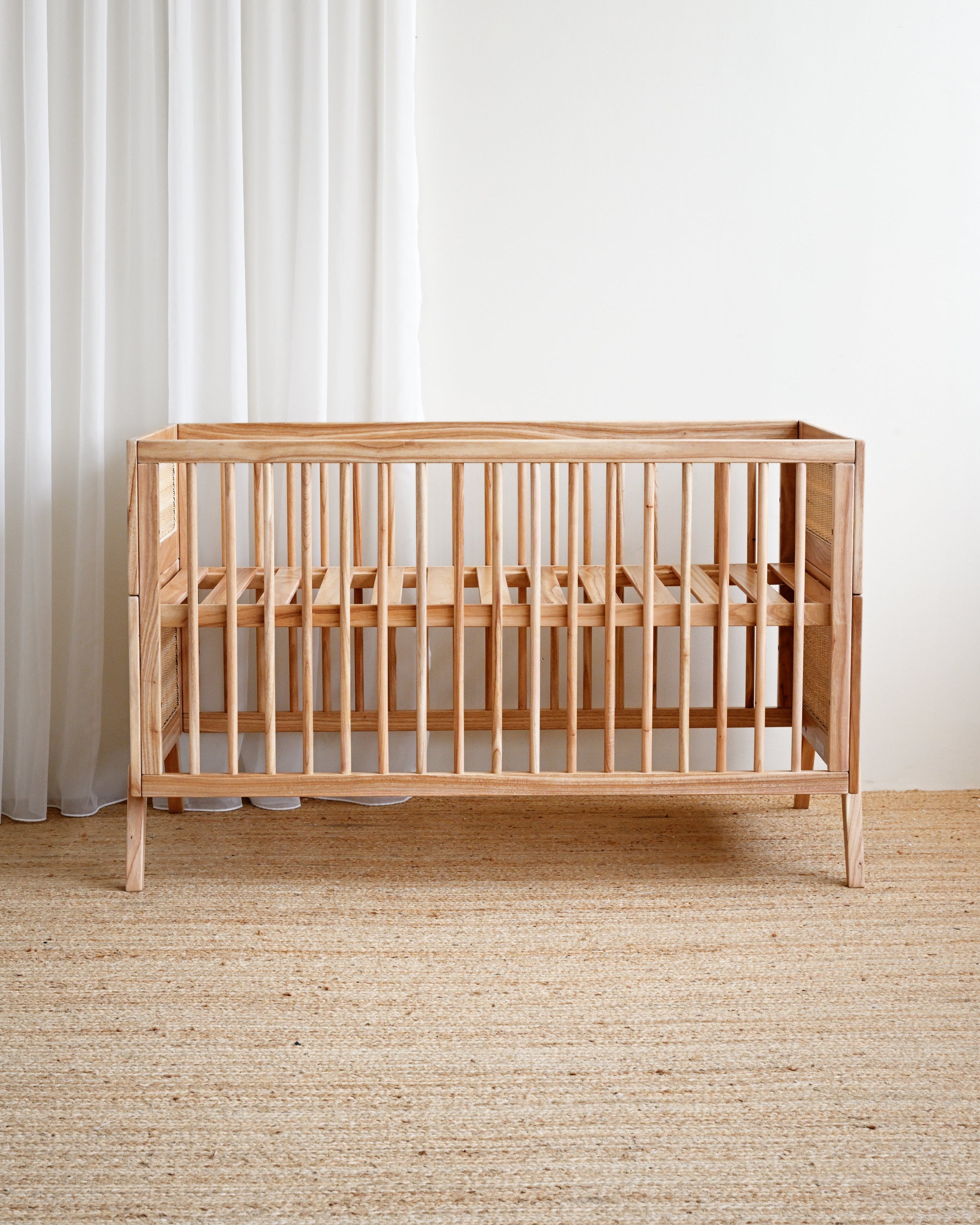 Wooden crib in a room with white curtains and a beige carpet.